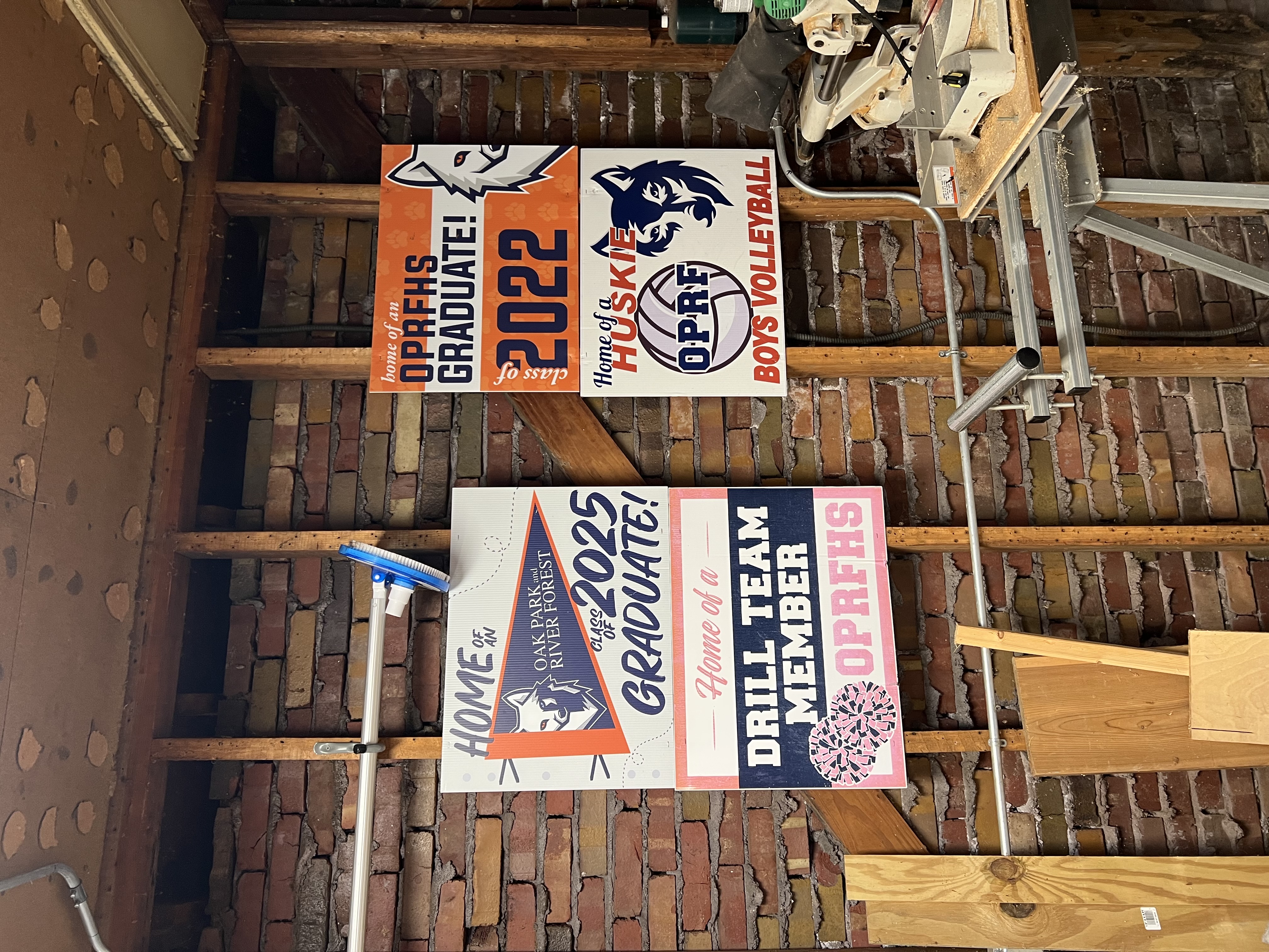 four yard signs celebrating the kids graduations and sports are nailed to the garage wall